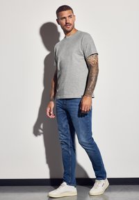 Graues Baumwoll-T-Shirt mit kurzen Ärmeln, kombiniert mit blauen Jeans und weißen niedrigen Sneakern. Glatte Textur, lässiger Schnitt.