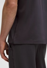 Tmavě šedé sportovní tričko vyrobené z hladkého, pružného materiálu, s podrobným prošitím a malým logem na lemu, spárováno s odpovídajícími šortkami.