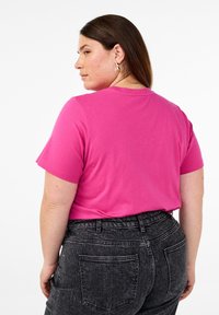 T-Shirt mit kurzen Ärmeln und Rundhalsausschnitt in leuchtendem Pink, aus weichem Stoff; kombiniert mit hochgeschnittenen schwarzen Jeans mit Gesäßtaschen.
