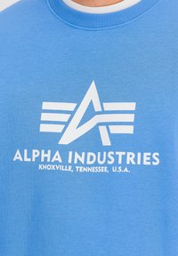 Plava dukserica s teksturiranim završetkom, koja sadrži bijeli logo s stiliziranim slovima i linijama. Uključuje tekst "Knoxville, Tennessee, U.S.A.".