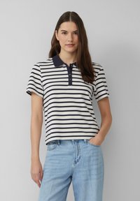 Marineblauwe en witte gestreepte poloshirt met kraag, korte mouwen en drieknops sluiting; gecombineerd met lichtblauwe jeans.
