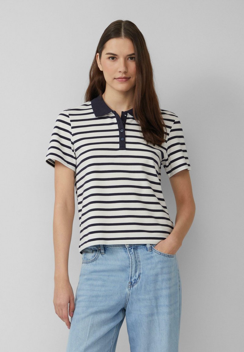 Marineblauwe en witte gestreepte poloshirt met kraag, korte mouwen en drieknops sluiting; gecombineerd met lichtblauwe jeans.