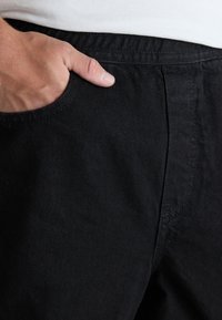 Pantalones de mezclilla negros con una textura suave, que cuentan con un bolsillo lateral y detalles de costura sutiles, destacando un diseño ajustado.