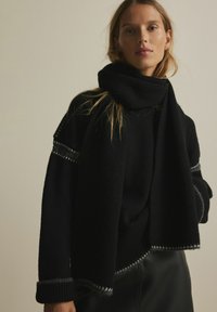 Schwarzer Strickpullover mit passendem Schal. Verfügt über strukturierter Stoff und kontrastierenden silbernen Akzenten an den Ärmeln und dem Saum.