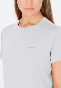 Ljusgrå atletisk t-shirt tillverkad av mjukt tyg, med rund hals och korta ärmar, med "ENDURANCE"-logotyp i diskret rosa.