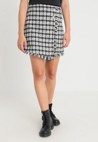 Zwart-wit geruite mini rok met franjes aan de onderkant en twee knopen aan de zijkant, gedragen met zwarte veterschoenen tot de enkel.