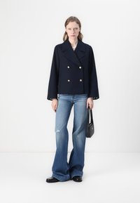 Marineblå dobbeltradet blazer med gyldne knapper og brede ærmer. Båret med slidte lysblå flared jeans og en sort håndtaske.