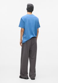 Zila kokvilnas T-krekliņš ar brīvu piegriezumu, saskaņots ar brīviem pelēkiem sporta biksēm un teksturētu pelēku cepuri. Melni apavi noslēdz apģērbu.