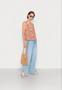 Top sem mangas com padrão floral em rosa, amarelo e verde. Combinado com jeans de perna larga azul claro, sandálias brancas e uma bolsa em bege trançada.