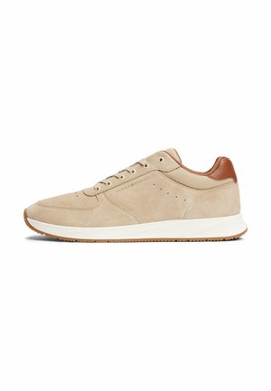 Baskets en daim beige avec des accents en cuir marron, semelle en caoutchouc blanc, matériaux texturés et détails perforés sur les côtés.