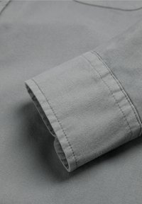 Nærbillede af gråt bomuldsstof med en foldet manchet, der viser syninger og en glat tekstur.