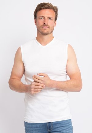 Witte mouwloze V-hals T-shirt van een zachte stof, slim fit ontwerp, gladde textuur, gecombineerd met blauwe denim jeans. Geen zichtbare patronen of accenten.