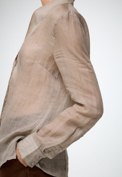 Camicia beige chiaro a maniche lunghe realizzata in tessuto trasparente con una vestibilità rilassata. I dettagli notevoli includono un colletto alto e polsini con bottoni.