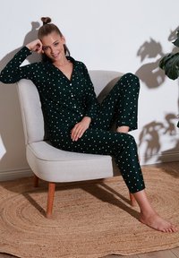 Ensemble de pyjama à pois verts en tissu doux, comprenant un haut à boutons et un pantalon assorti, présenté sur une chaise de couleur claire.