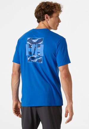 Modrá bavlněná tričko s kulatým výstřihem, které má na zadní straně grafický design se zubatými vzory a logem "HH".