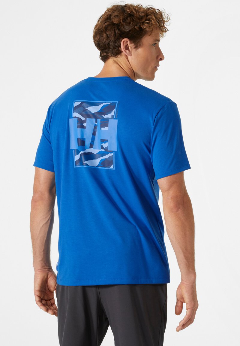 Modrá bavlněná tričko s kulatým výstřihem, které má na zadní straně grafický design se zubatými vzory a logem "HH".