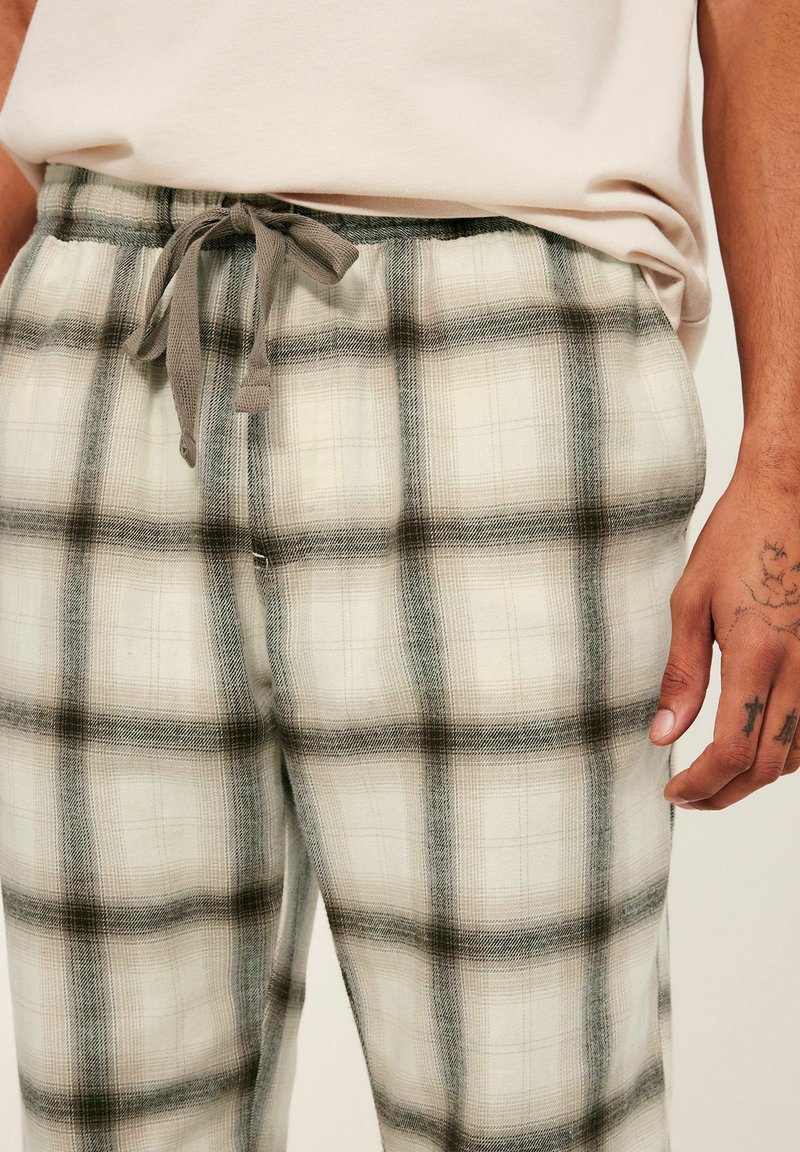 Spodnie w kratę w odcieniach jasnego beżu, szarości i czerni. Wykonane z miękkiego materiału, mają elastyczny pas z szarym sznurkiem oraz boczne kieszenie.