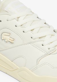Zapatilla blanca de cuero con acentos de malla, punta redonda, cordones planos y una suela media texturizada. Presenta un logo de cocodrilo elevado en el costado.