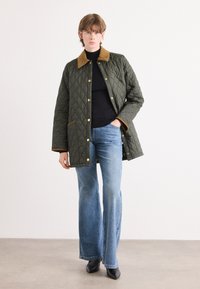 Groene gewatteerde jas met een bruin corduroy kraag, gouden drukknopen en zijzakken, gecombineerd met uitlopende blauwe spijkerbroeken en zwarte enkellaarsjes.