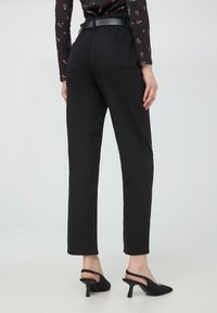 Jeans neri a vita alta con taglio dritto, dotati di due tasche posteriori e un tessuto dalla superficie liscia. Abbinati a scarpe slingback nere.