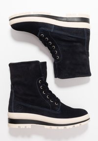 Botas de tobillo de ante azul marino con herrajes negros, suela de goma blanca, diseño con cordones y costuras en contraste. Parte superior texturizada para un mejor agarre.