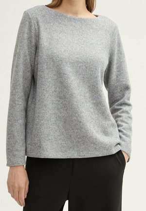 Maglietta grigia a maniche lunghe con scollo rotondo. Tessuto morbido e testurizzato con un sottile motivo a macchie. Abbinata a pantaloni neri, vestibilità rilassata.