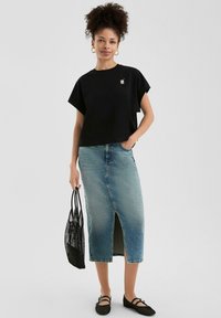 Must have lühikeste varrukatega must crop top väikese logoga, millele on kombineeritud helesinine denim midi seelik ees oleva lõhikuga, must võrkkott ja mustad lamedad jalanõud.