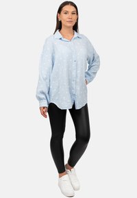 Lichtblauwe overhemd met witte stippen, lange mouwen en een losse pasvorm, gecombineerd met zwarte legging en witte sneakers.