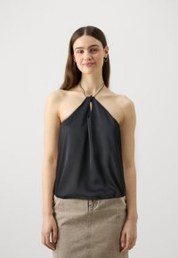 Mustmust halter-top mustaava kaelus ja pehme drapeering, kombineeritud beežist denims�ärgiga, esitledes neutraalse tausta ees.