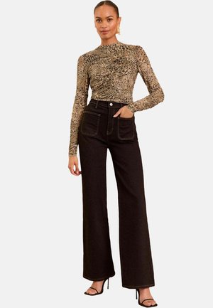 Halenka s leopardím potiskem a dlouhým rukávem, doplněná o černé široké kalhoty s vysokým pasem. Outfit doplňují černé sandály na vysokém podpatku a zlaté náušnice.