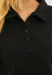Camiseta polo negra con cuello, que presenta una botonera con cuatro botones negros y una tela de algodón texturizada.