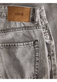 Grå denimjeans med en läderlapp märkt "JJXX." Funktioner inkluderar sydda sömmar, en bakficka och en standard midjedesign.