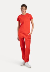 Conjunto atlético rojo de dos piezas que incluye una camiseta de cuello redondo y mangas cortas, y pantalones con cintura elástica, combinado con zapatillas blancas.
