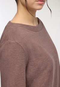 Brązowy, miękki sweter dzianinowy z szerokim dekoltem i luźnym krojem, z gładką powierzchnią i detalami szwów na ramionach.