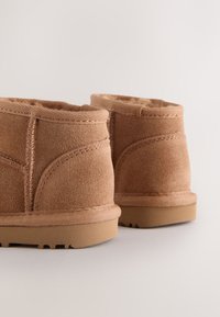 Beige Wildleder-Stiefeletten mit weichem Futter, abgerundeter Form und Gummisohle. Mit sichtbaren Nähten und einem flachen, unauffälligen Design.
