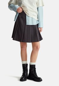 Gonna plissettata grigia scura, sovrapposta a una camicia crema e blu. Stivali neri stringati con suole spesse e calzini a coste bianchi.
