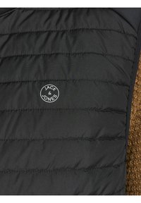 Czarna pikowana kamizelka z fakturą przeszyć oraz okrągłym logo Jack & Jones, z brązowym, pluszowym materiałem po boku dla kontrastu.