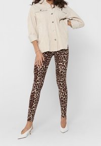 Leggings imprimé léopard en tissu extensible associés à une chemise beige surdimensionnée boutonnée et à des chaussures blanches à talons.