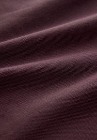 Nahaufnahme eines tief strukturierten, glatten Stoffes in gedämpfter Pflaumenfarbe mit weichen Falten, die sanfte Schatten erzeugen.