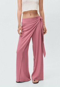 Brede, wikkelstijl broeken van zacht, gestructureerd rozenstof met een strikaccent op de taille. Heeft een losse pasvorm en een vloeiende drape.