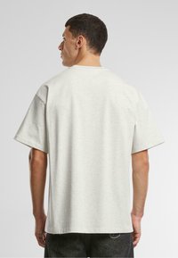 Tricou din bumbac gri deschis, cu mâneci scurte, croială lejeră și guler tip rotund. Textură netedă, design simplu fără modele sau accente.