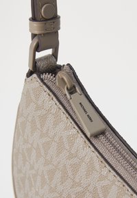 Sac à main beige à motifs avec une fermeture éclair, des accents en cuir et une étiquette Michael Kors. Présente une texture lisse et une forme géométrique incurvée.