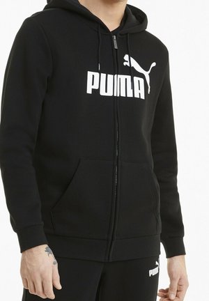 Mand iført sort Puma hættetrøje med frontlynlås og kængurulommer, kombineret med matchende sorte Puma bukser.