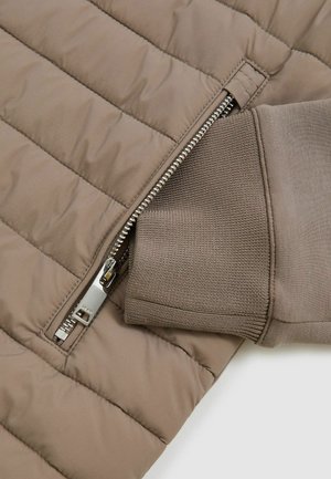 Jachetă maro matlasată cu fermoar și manșete din tricot. Prezintă secțiuni netede, captusite și un sistem de închidere cu fermoar metallic. Material moale, texturat.