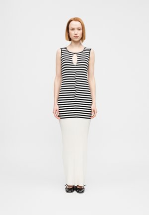 Črno-bela prugasta brezrokavnik z izrezom, kombiniran z dolgo, rebrasto kremasto krilo in črnimi zaprti čevlji.