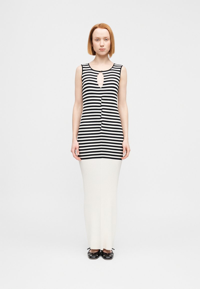 Μπλούζα χωρίς μανίκια με μαύρες και άσπρες ρίγες και λεπτομέρεια κοψίματος στην περιοχή του ντεκολτέ, συνδυασμένη με μακριά, ριμπ ροζέ φούστα και μαύρα κλειστά παπούτσια.