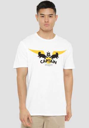 Young man wearing a white T-shirt with yellow wings, black badger silhouettes, "CAPTAIN" and "HUFFLEPUFF" text on front.