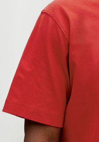 Punane lühikeste varrukatega T-särk sileda tekstuuriga, sirge lõike ja õmmeldud servadega. Kangas näeb välja kerge ja hingav.