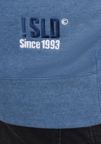 Felpa blu con testo ricamato: "!SLD ©" in blu scuro e "Since 1993" in bianco. Orlo e polsini a coste, texture morbida.