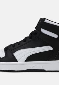 Czarny wysoki sneaker z białymi akcentami, wykonany z materiału skórzanego, okrągły nos, sznurowadła i teksturowana podeszwa; ma logo PUMA z boku.